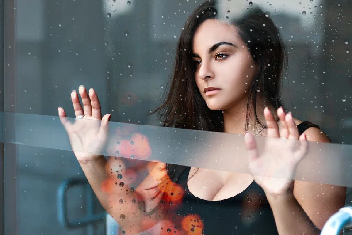Portrait of a thoughtful woman standing behind a glass window on a rainy day in Santos, Brazil.