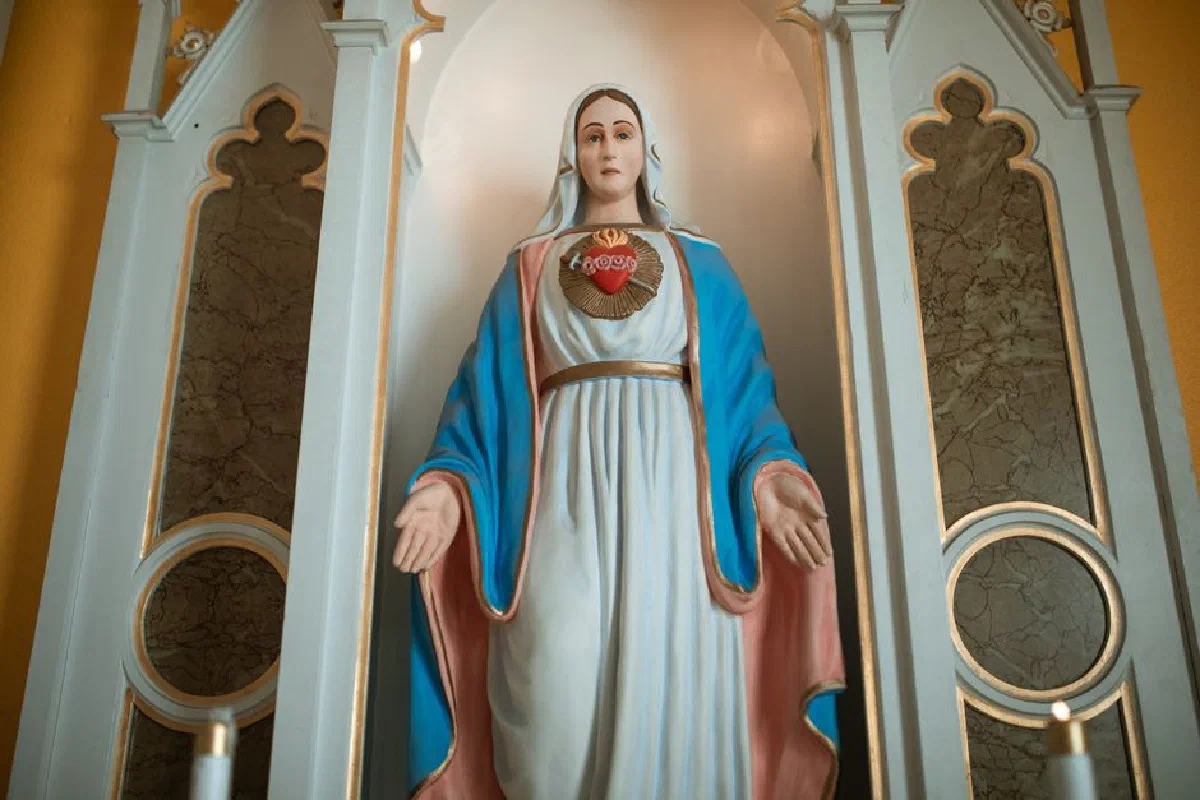 Statue of Virgin Mary with sacred heart in a church setting, symbolizing devotion.