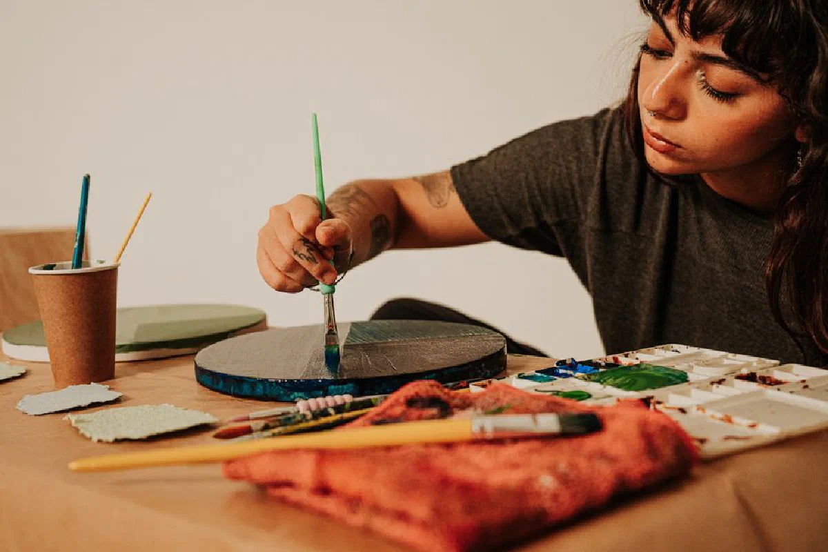 Focused young woman artist painting an artwork indoors using acrylic colors and brushes.