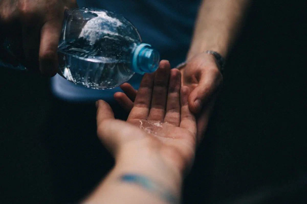 Close-up shot of water being poured from a plastic bottle into open hands, emphasizing cleanliness and refreshment.
