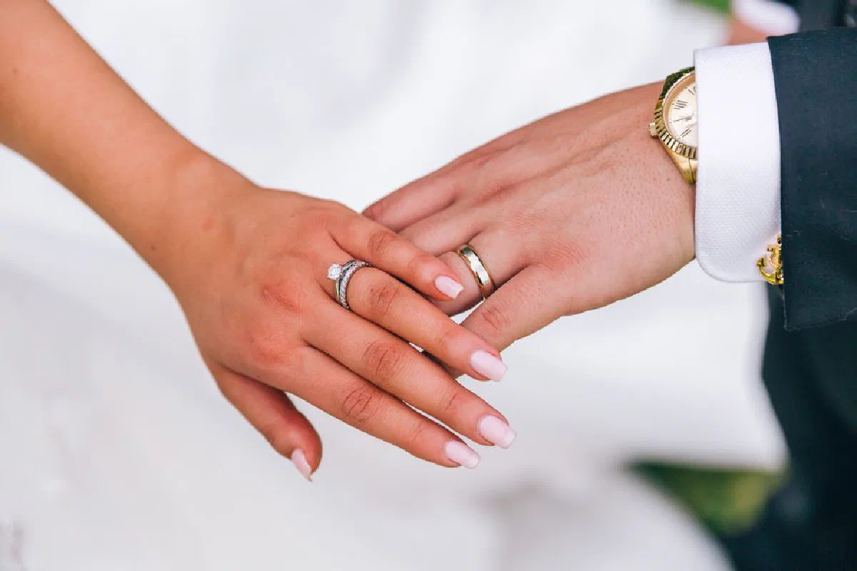 Elegant photo of newlyweds holding hands, showcasing wedding rings and manicured nails.
