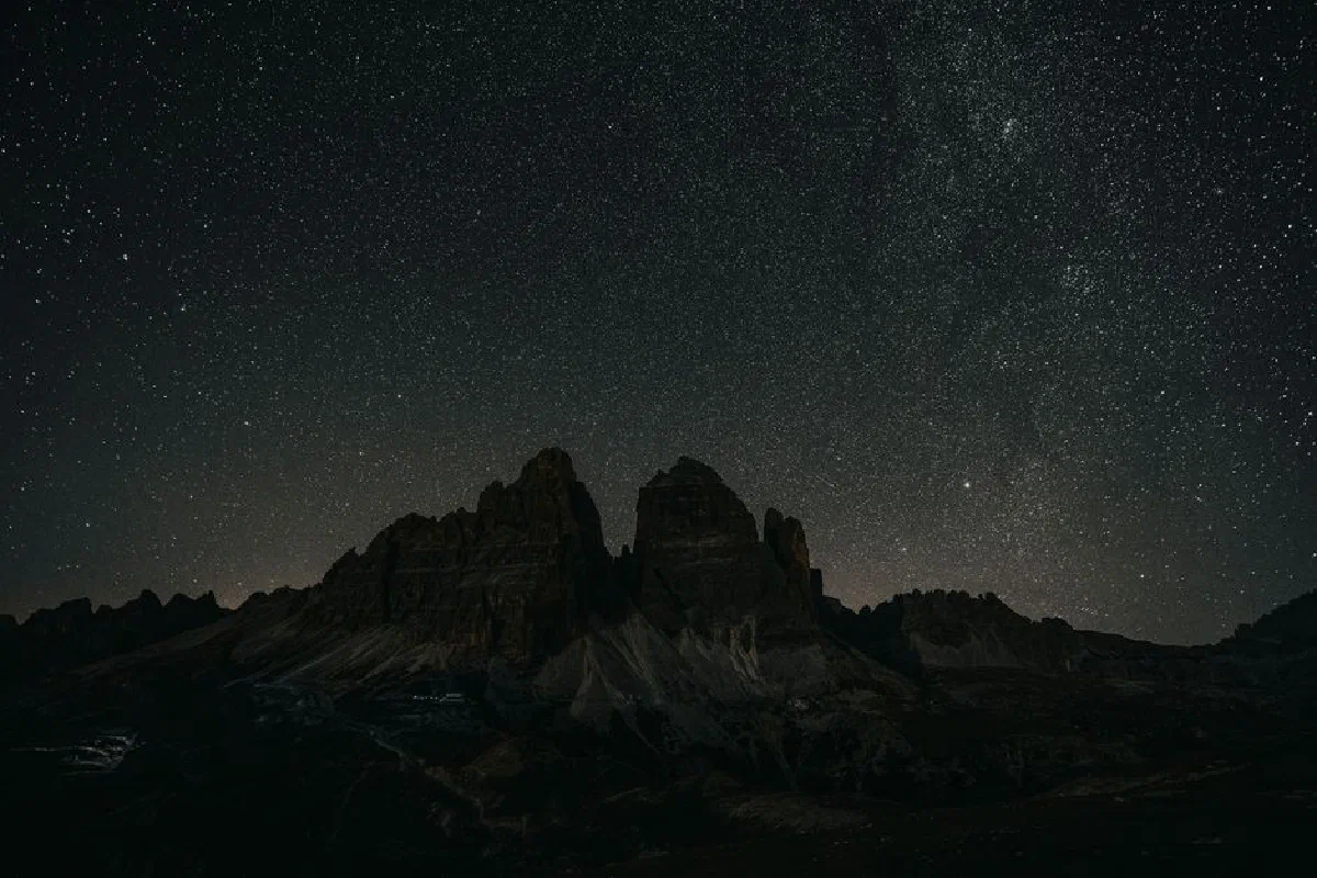 A breathtaking view of a star-filled sky over a jagged mountain range at night.