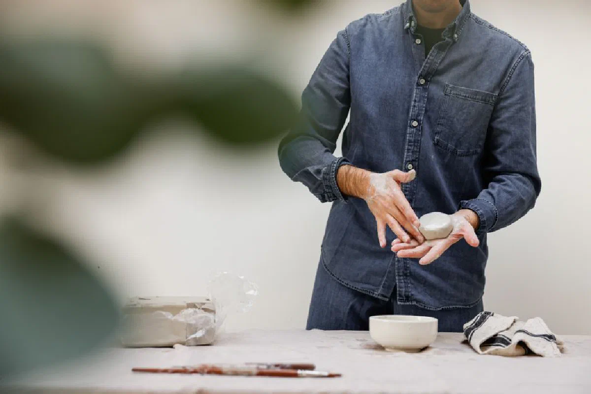 Man in denim shaping clay in a ceramics workshop, demonstrating creative processes.