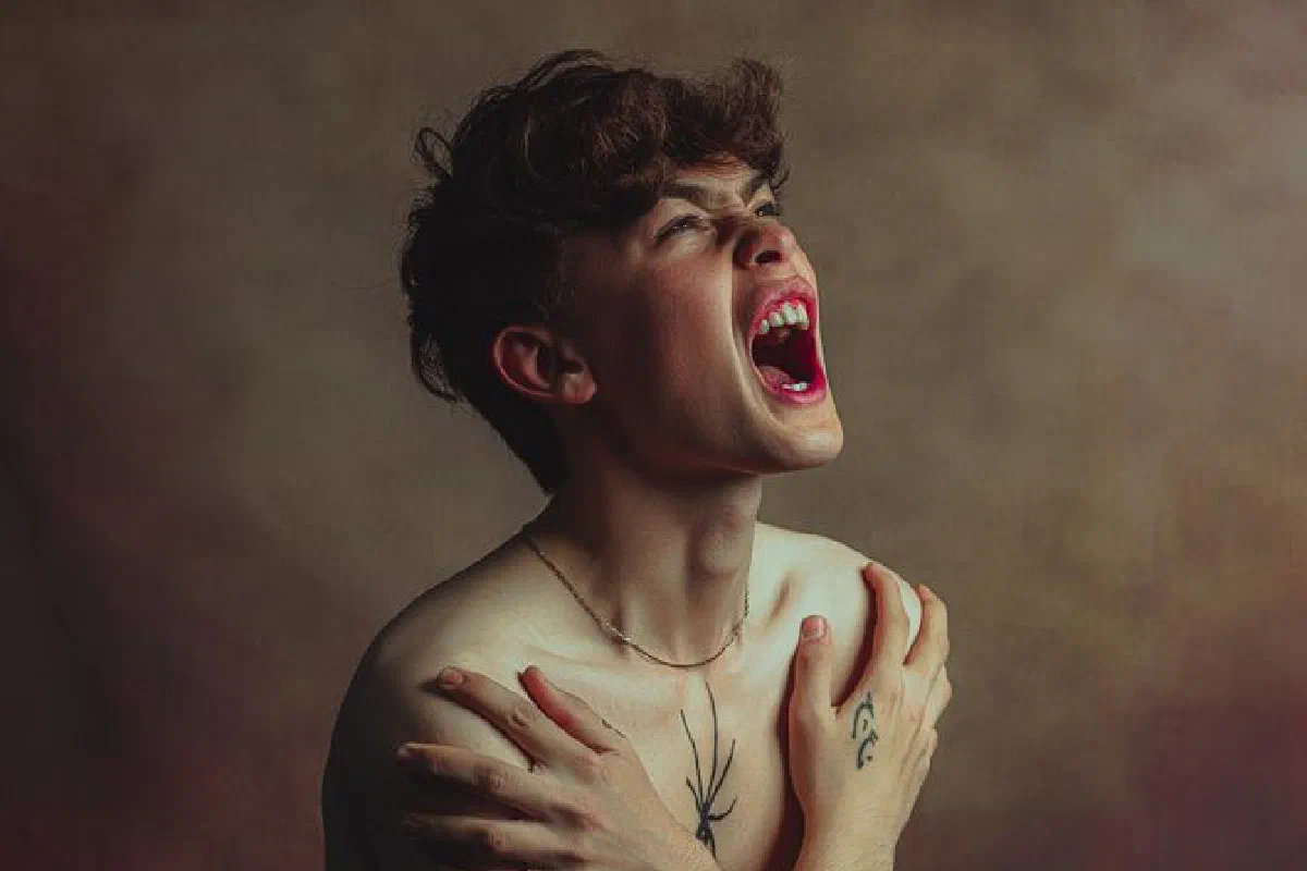 Dramatic close-up portrait of a tattooed young man shouting with intense expression.