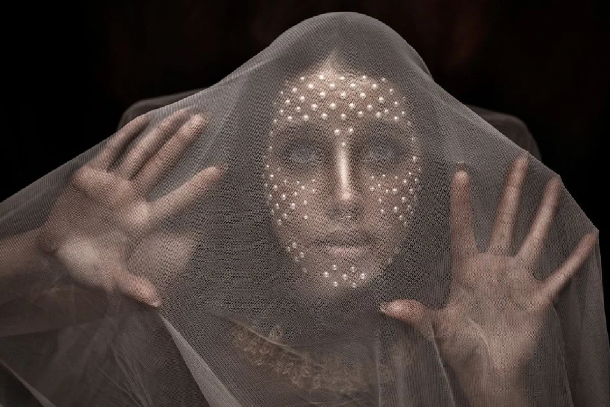 Mysterious art portrait of a person behind a mesh veil with dots lighting their face.