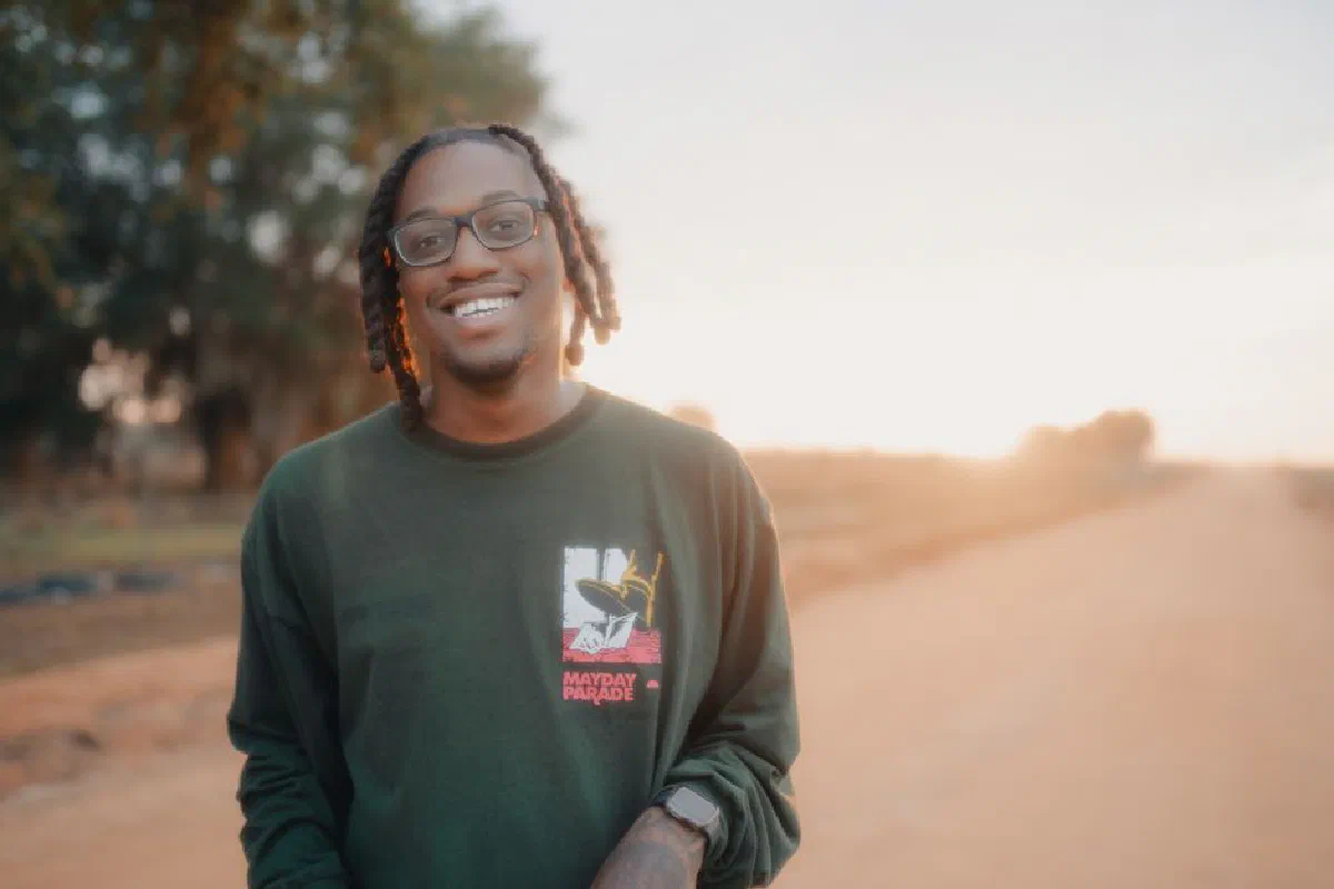 Casually smiling man with eyeglasses outdoors at sunset.