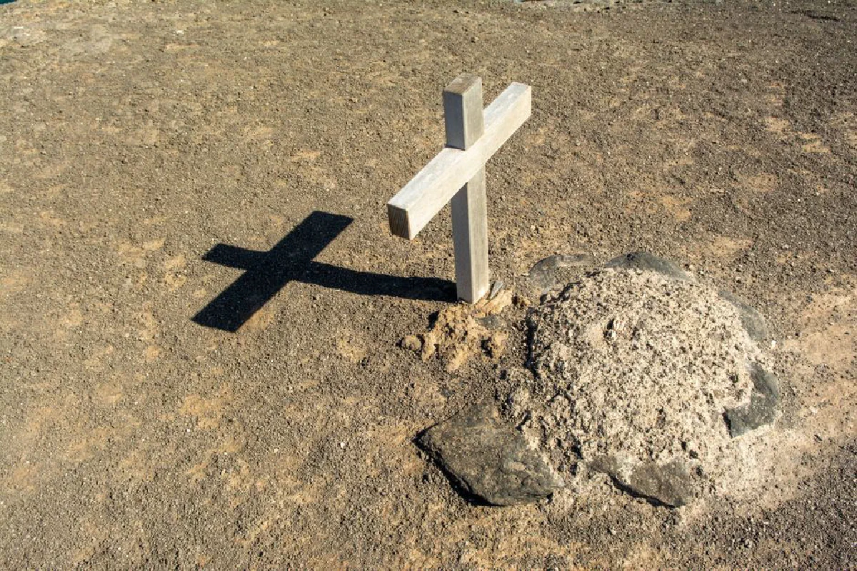 A solitary wooden cross casting a shadow on an arid grave site, symbolizing solitude and spirituality.