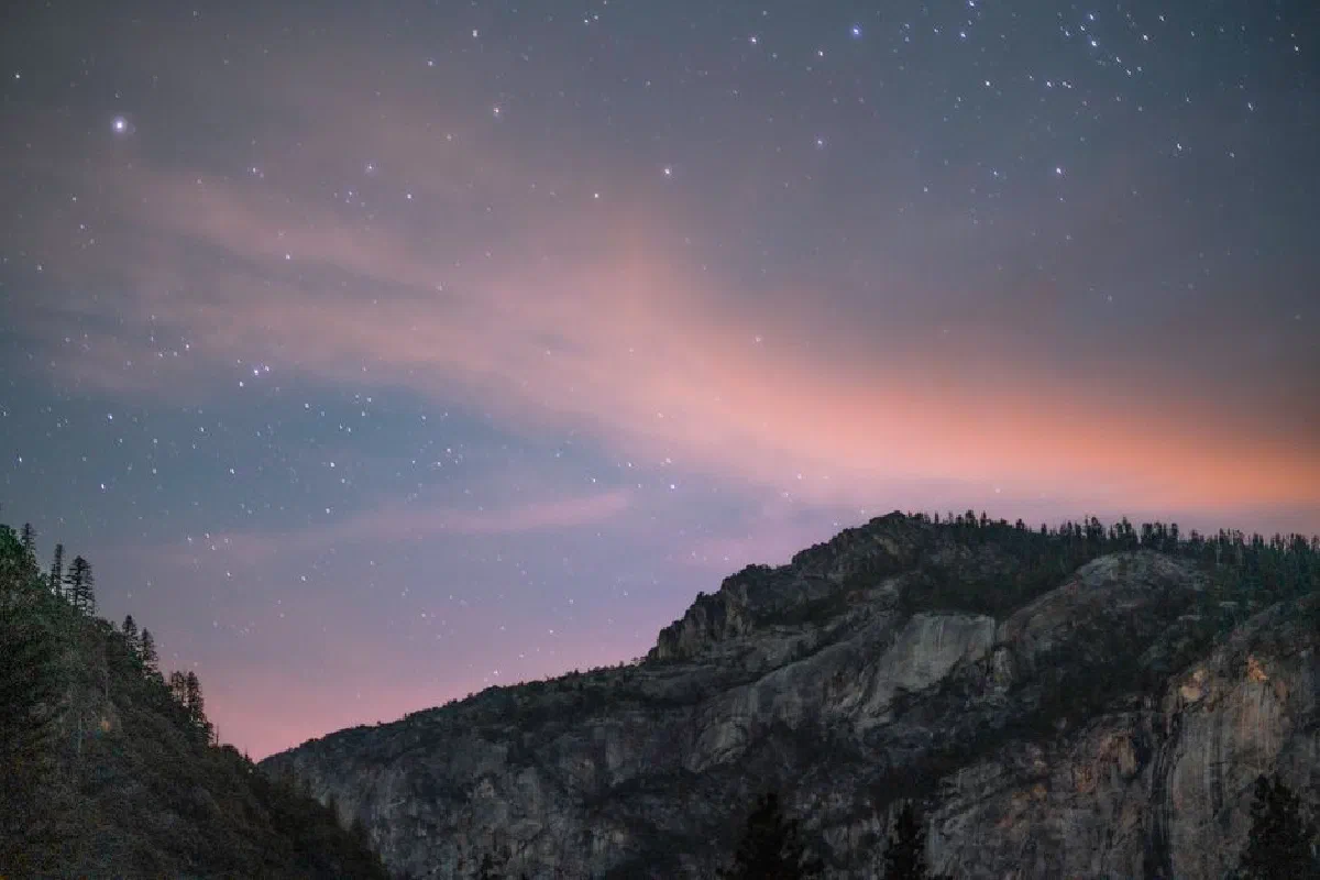 A serene view of a starlit night sky over a rugged mountain landscape.