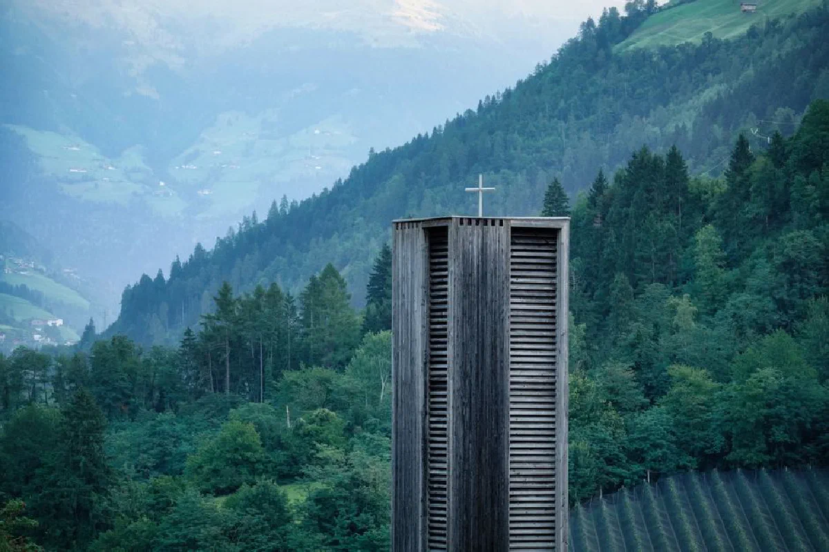 A contemporary wooden church tower set against the lush greenery of Saltaus, Italy's Trentino-Südtirol region.