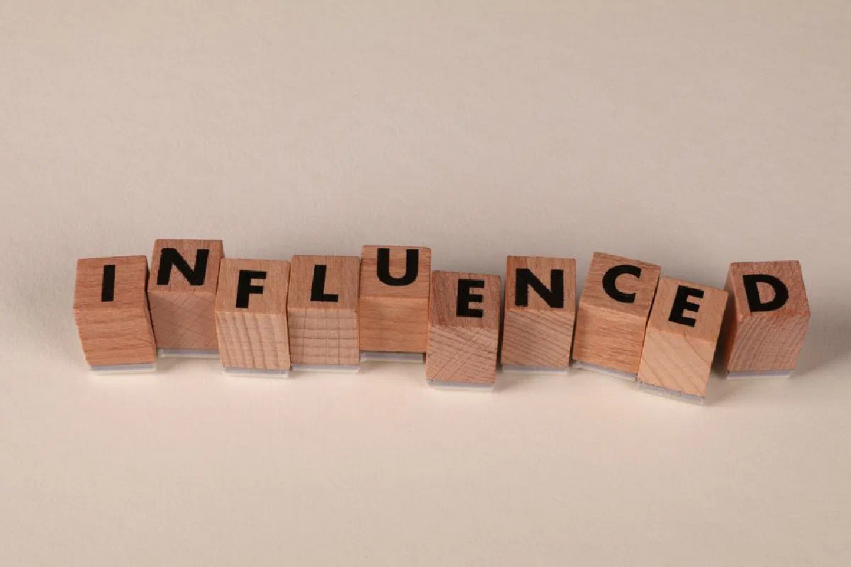 Wooden blocks with letters spelling 'Influenced' arranged on a beige surface.