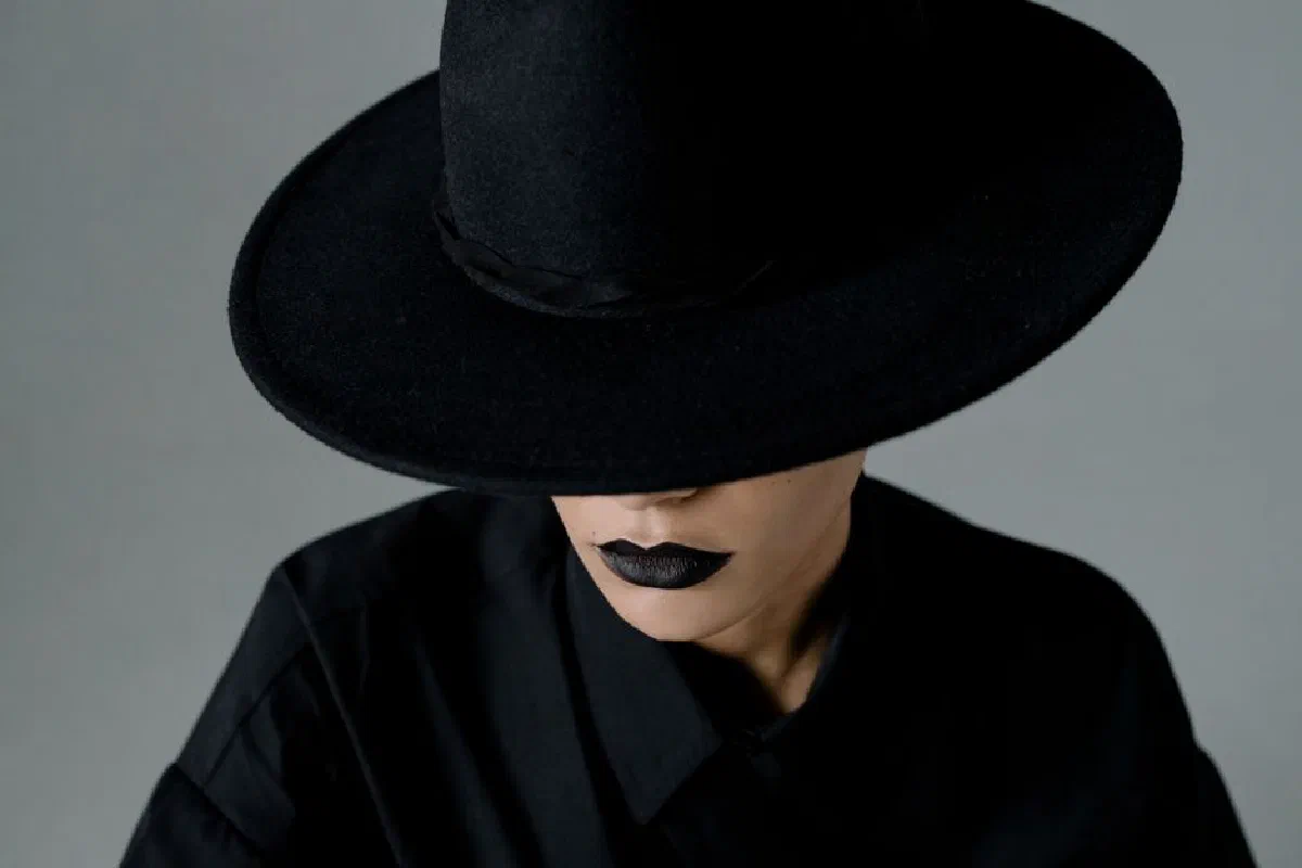 Portrait of a woman in a wide-brimmed black hat, wearing black lipstick, creating a mysterious vibe.