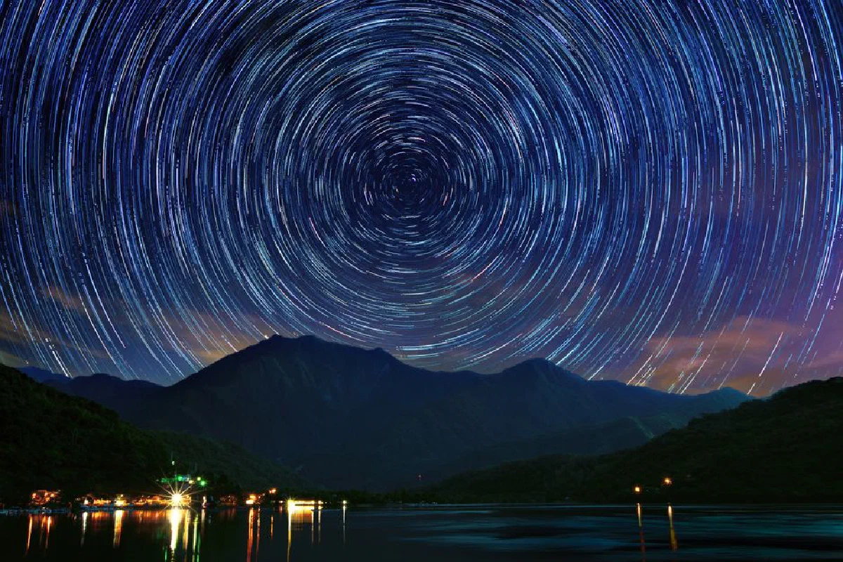 Dazzling star trails swirl above Taiwan's serene mountain landscape at night.
