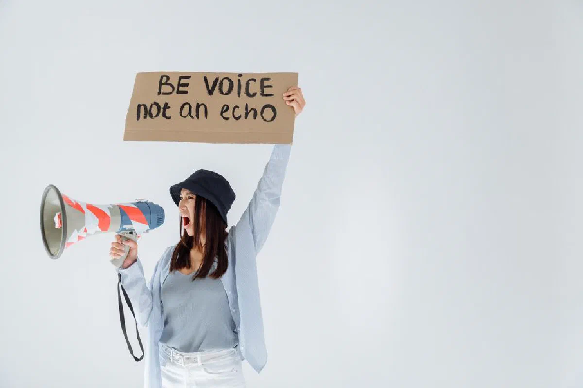 Empowered woman shouts message through megaphone, holding sign that reads 'Be voice, not an echo'.