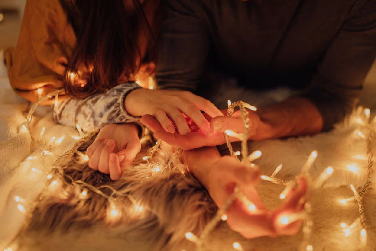 Close-up of couple holding hands illuminated by string lights, evoking warmth and love.