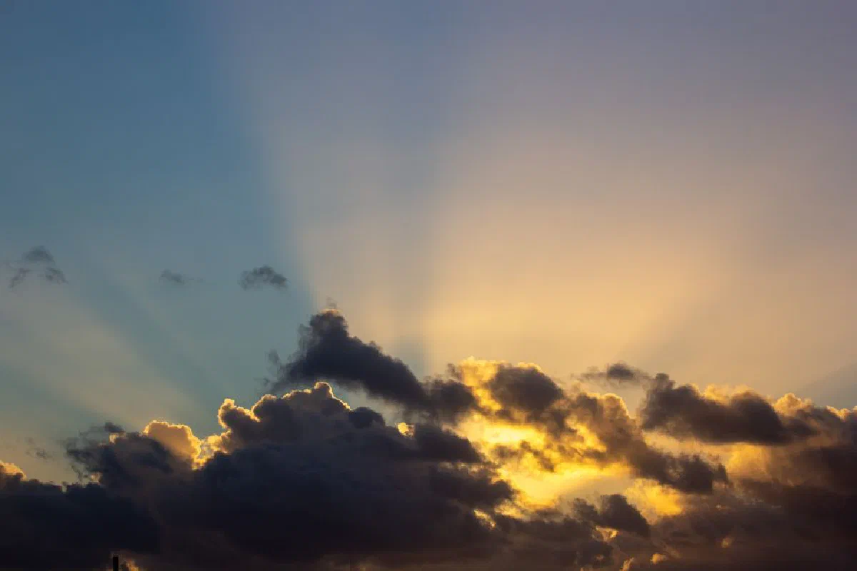Golden sun rays break through dark clouds at sunset, creating a dramatic sky scene.