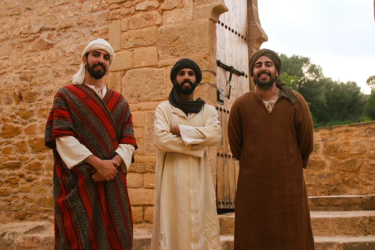 Three men in traditional Moroccan attire stand before an ancient stone fortress, showcasing cultural heritage.