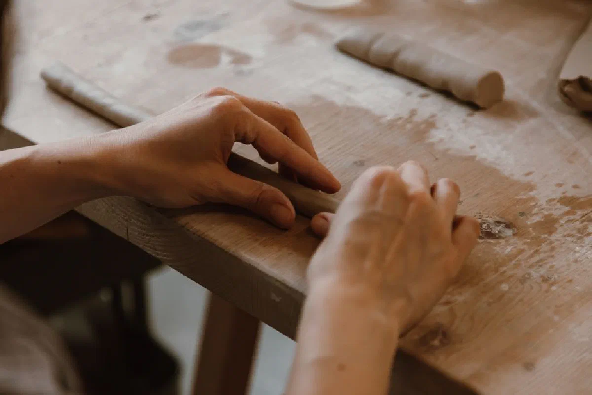 Close-up of a person shaping clay on a wooden table, showcasing handcrafting skills.