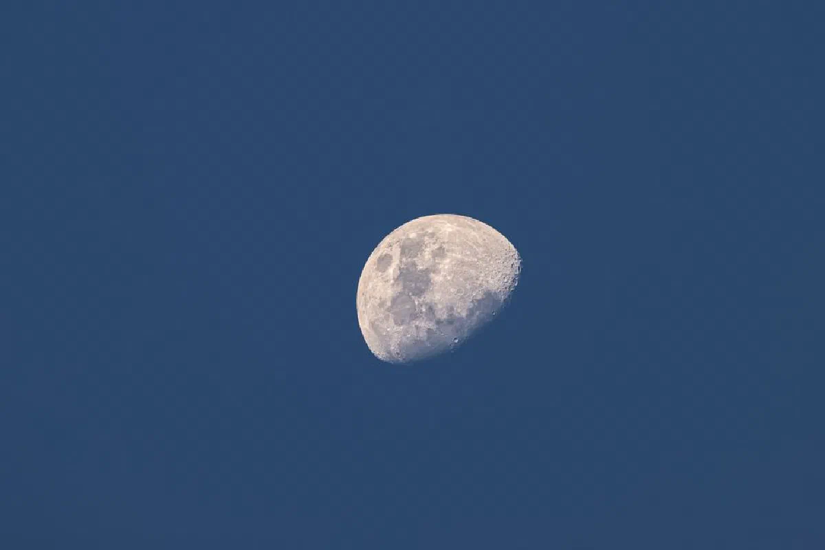 Close-up of the waxing gibbous moon captured against a clear blue sky, showcasing intricate lunar details.