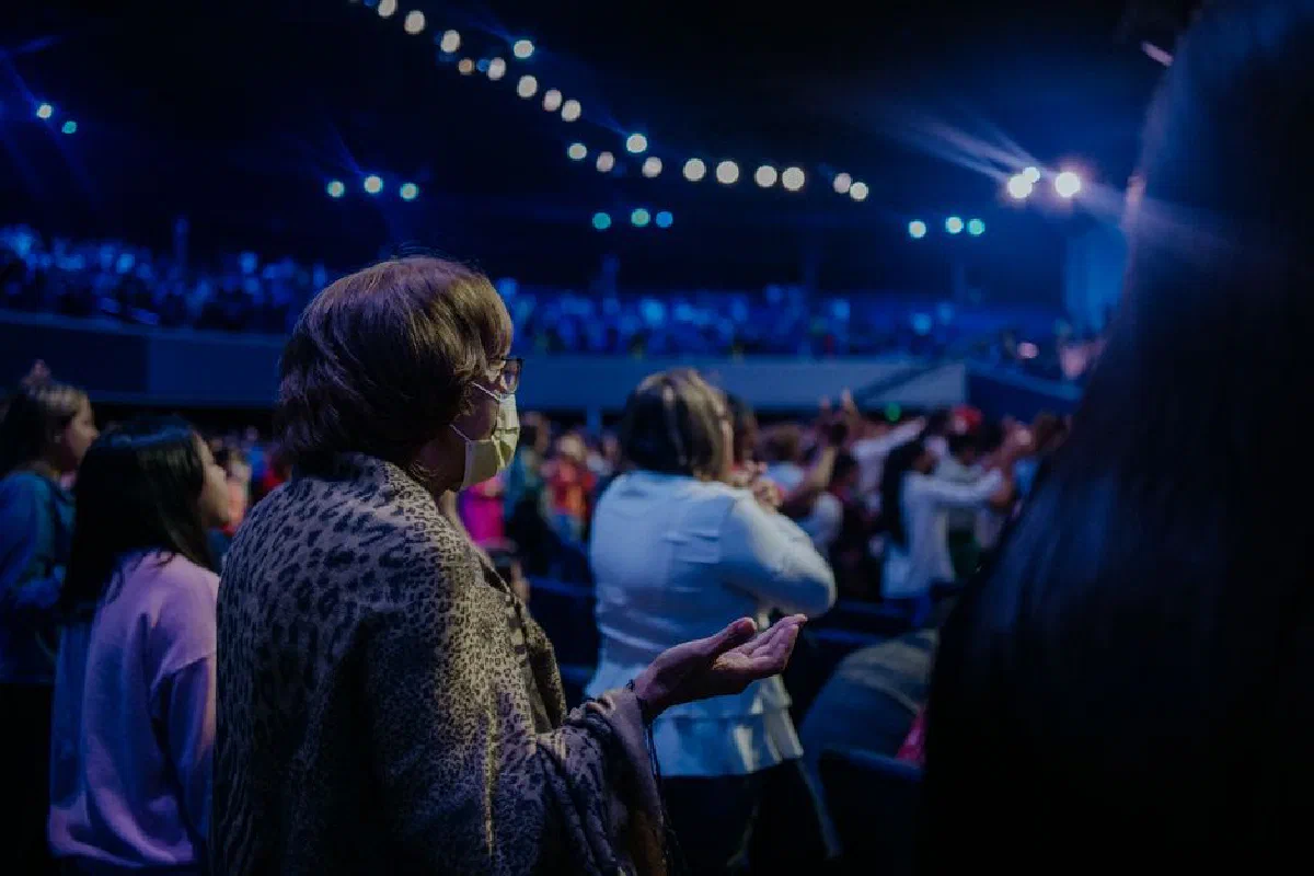 A spiritual gathering with people praying and worshiping under bright indoor lights.