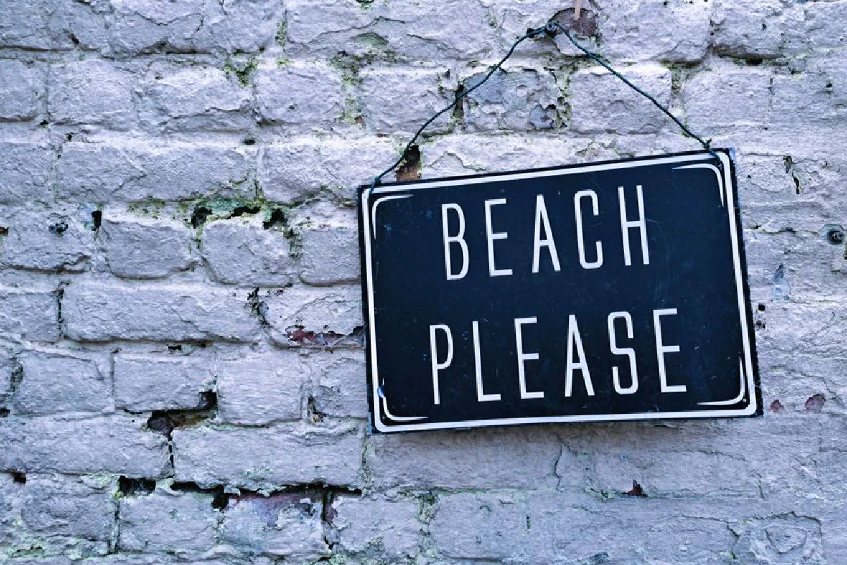 Close-up of a hanging 'Beach Please' sign on a rustic white brick wall. Ideal for decor themes.
