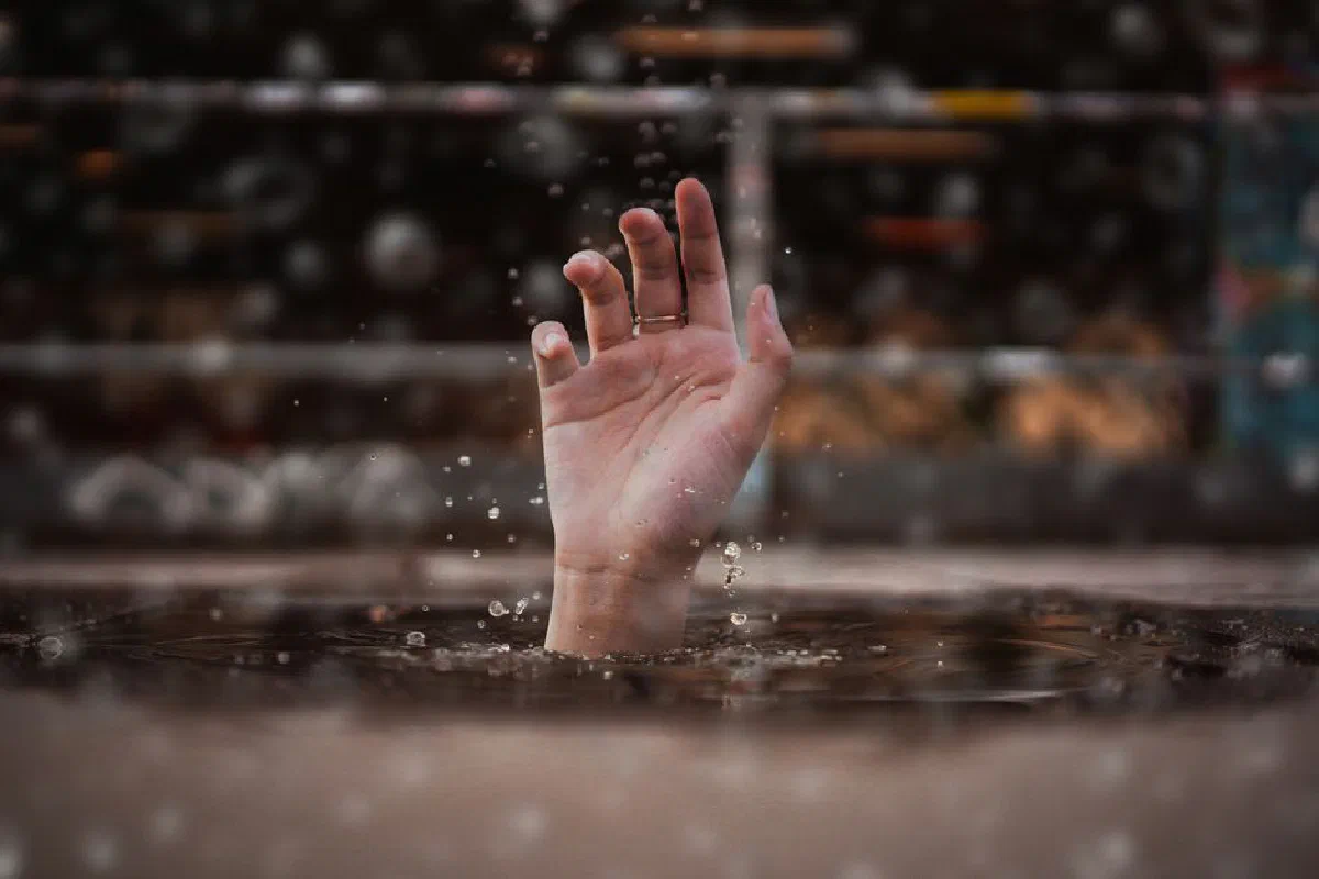 A single hand emerges from water, symbolizing a cry for help amidst a rainy setting.
