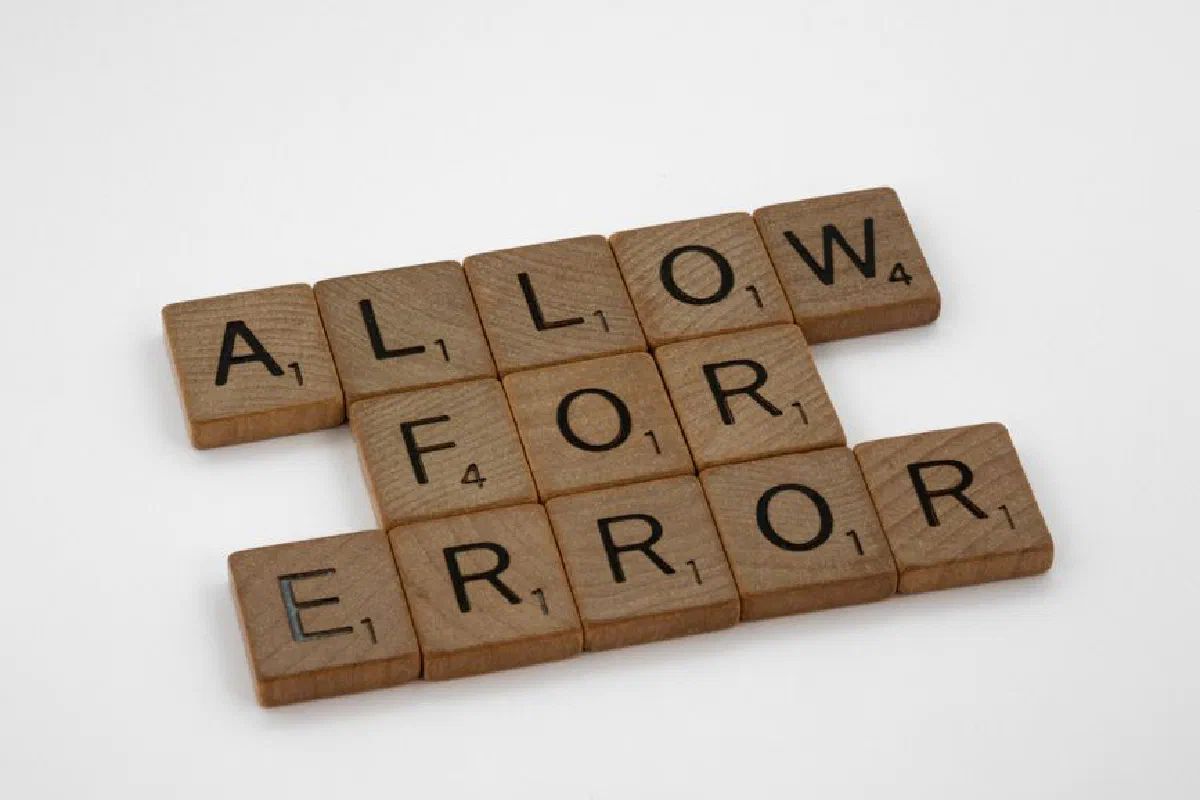Wooden Scrabble tiles spelling 'Allow for Error' on a white surface.