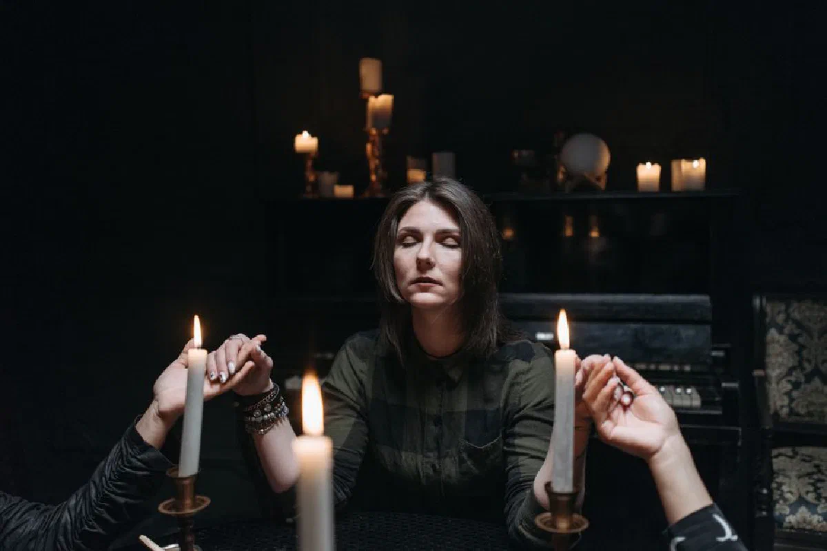 Mystical scene of a woman holding hands during a candlelit ritual, full of mystery.