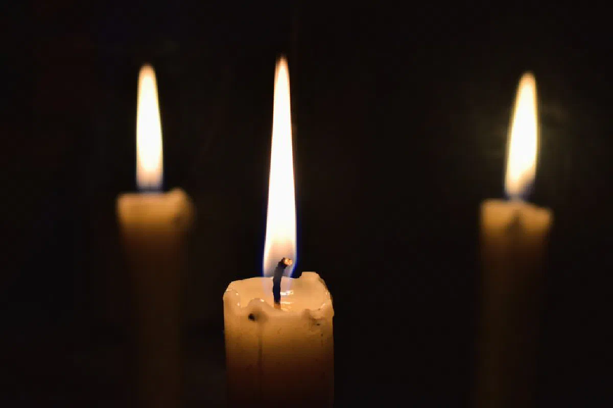 Three lit candles casting a warm glow in the darkness, creating a serene and contemplative atmosphere.