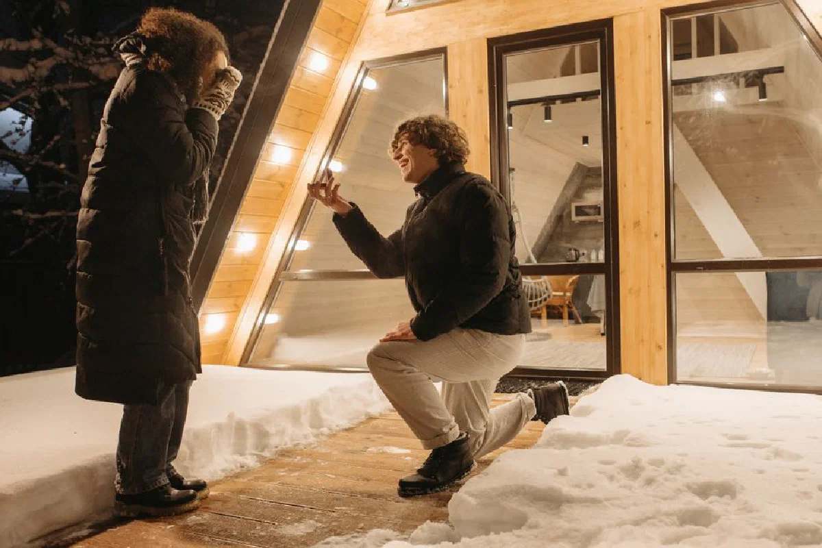 A romantic winter marriage proposal outside a cozy cabin amid snow and lights.