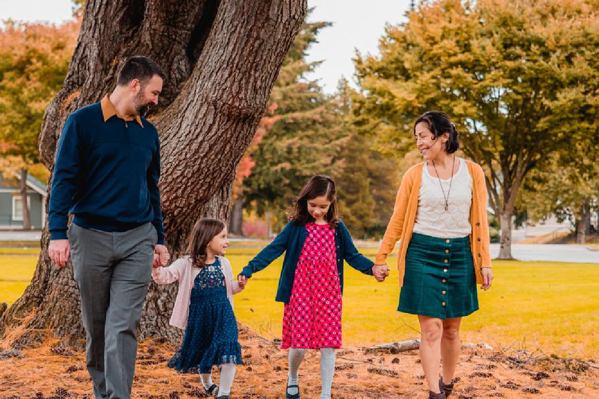 A family of four holding hands while walking together in a vibrant autumn park.