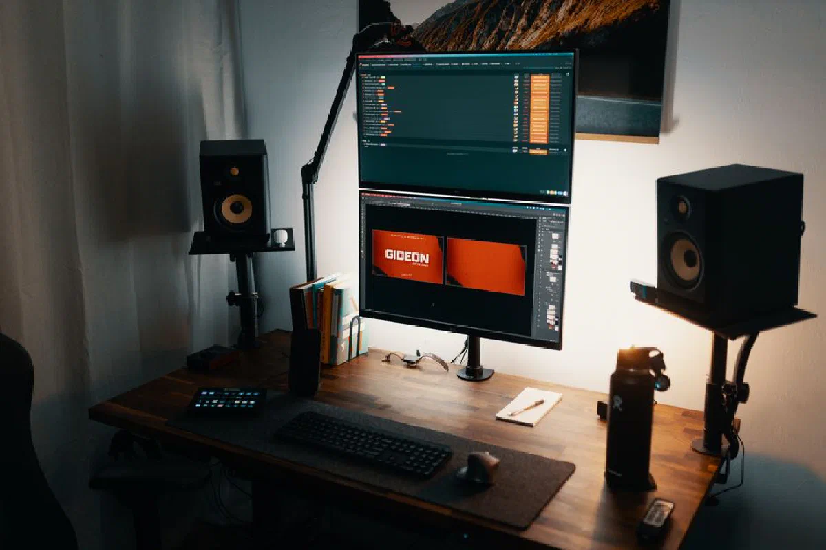 A well-lit modern workspace featuring dual monitors, speakers, and a tidy desk setup.