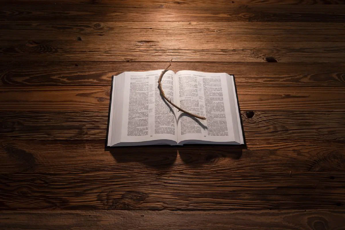An open Bible resting on a wooden table with a stick placed on its pages, illuminated by warm light.
