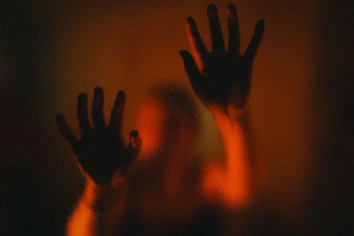 Mysterious silhouette of hands on frosted glass with dramatic red lighting.