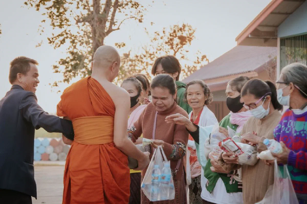 A group of locals interacting with a monk, exchanging goods outdoors during the day.