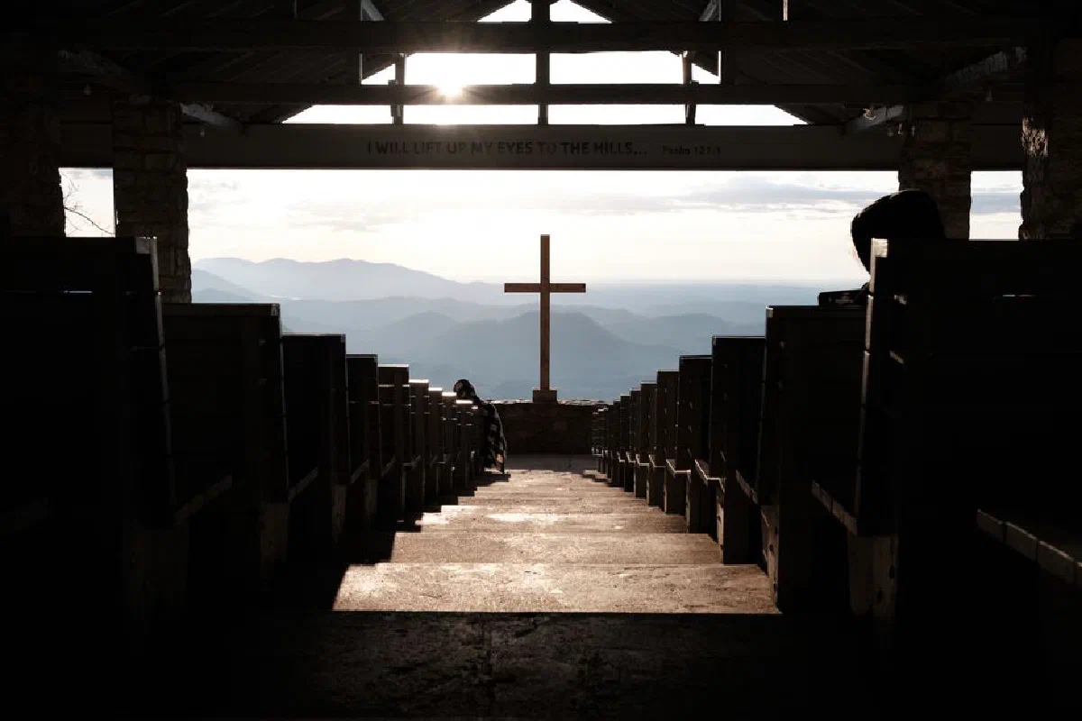 A serene church interior with a cross and mountain view at sunset, offering tranquility.