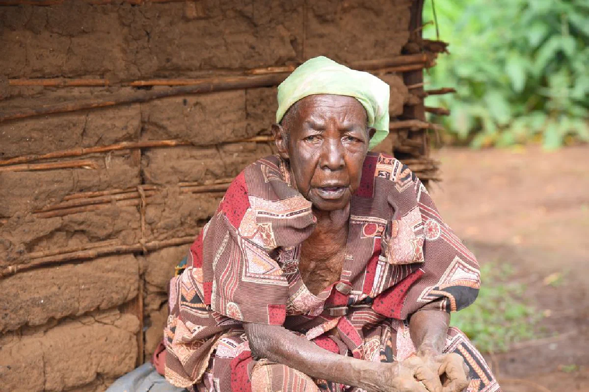 Portrait of an elderly Ugandan woman in traditional tribal attire, seated outdoors.