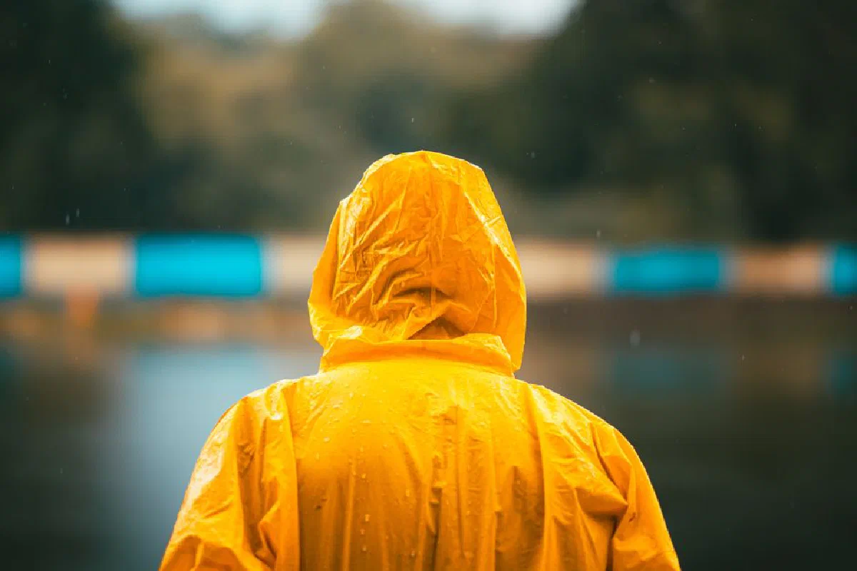 Person in a vibrant yellow raincoat standing by a calm lake on a rainy day.