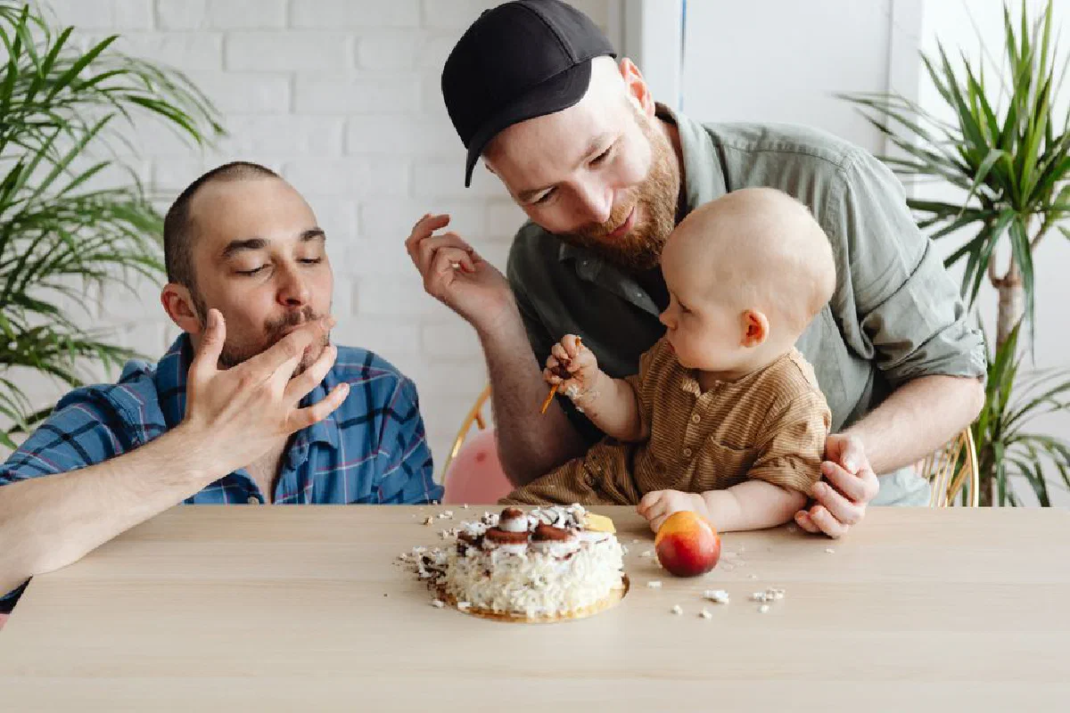 A joyful moment capturing a baby with two men celebrating a birthday indoors.