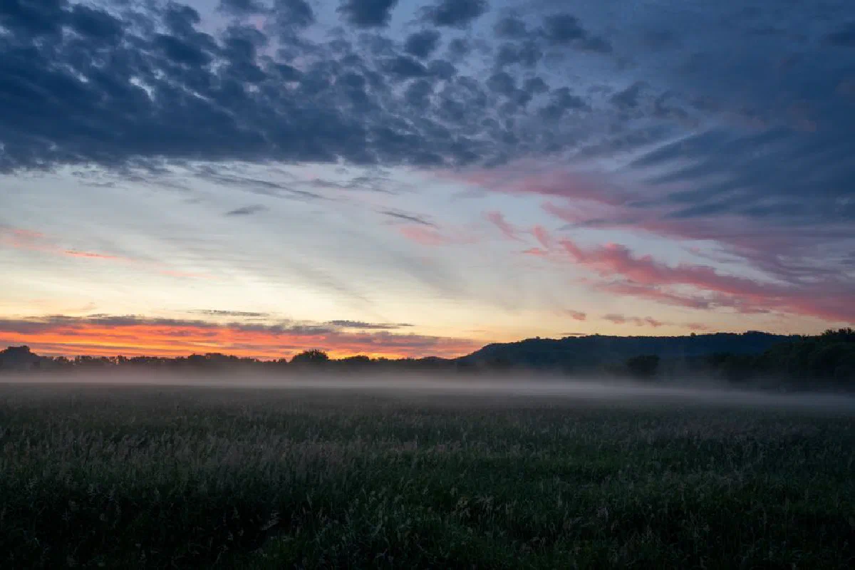 A tranquil sunset over a misty field in Modena, WI, with vibrant colors and cloud patterns.