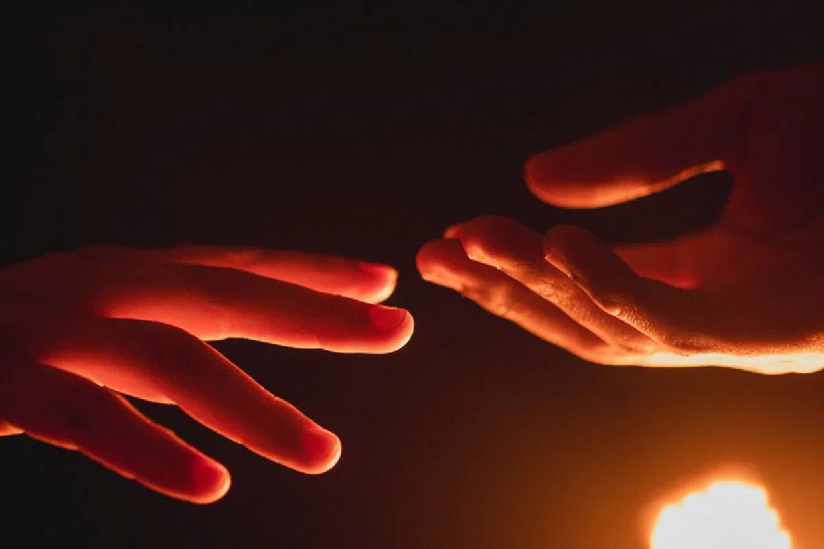 A close-up of two hands reaching towards each other in warm, glowing light.
