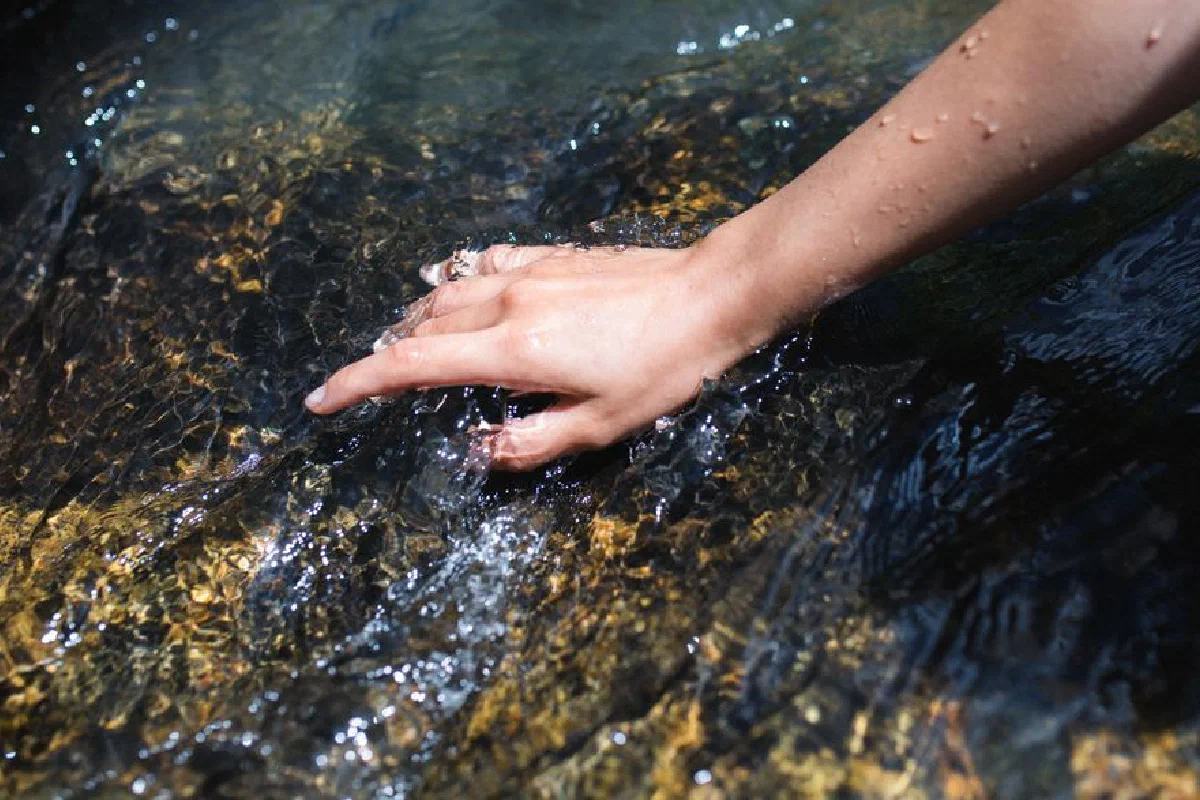 A close-up of a hand touching the clear water of a flowing stream, evoking freshness.