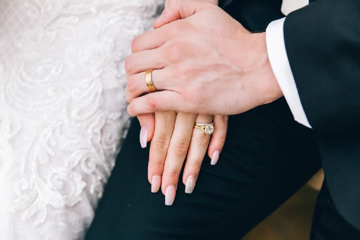 Close-up of a couple's hands during a wedding, showing elegant rings and bridal attire.