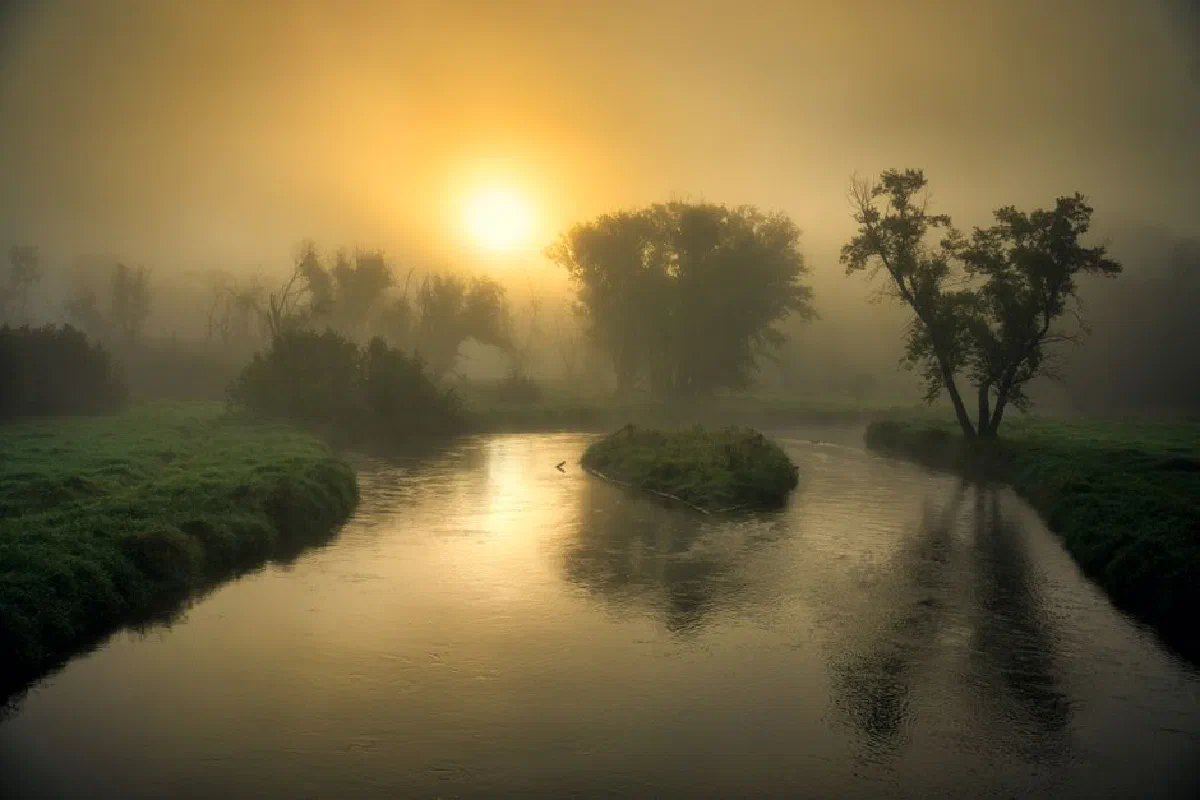 A tranquil sunrise casting golden hues over a misty river in Tell, Wisconsin.