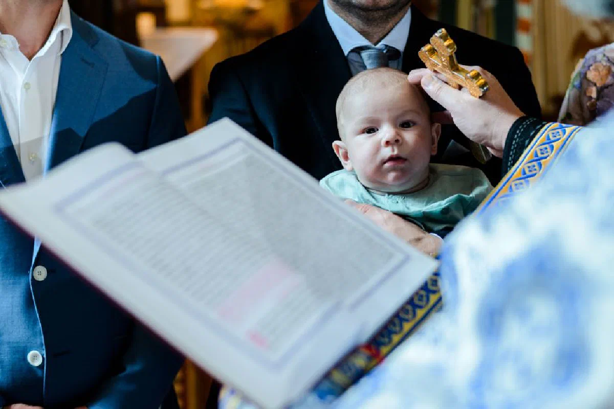 A Romanian baptism ceremony showing a priest blessing a baby with holy cross.