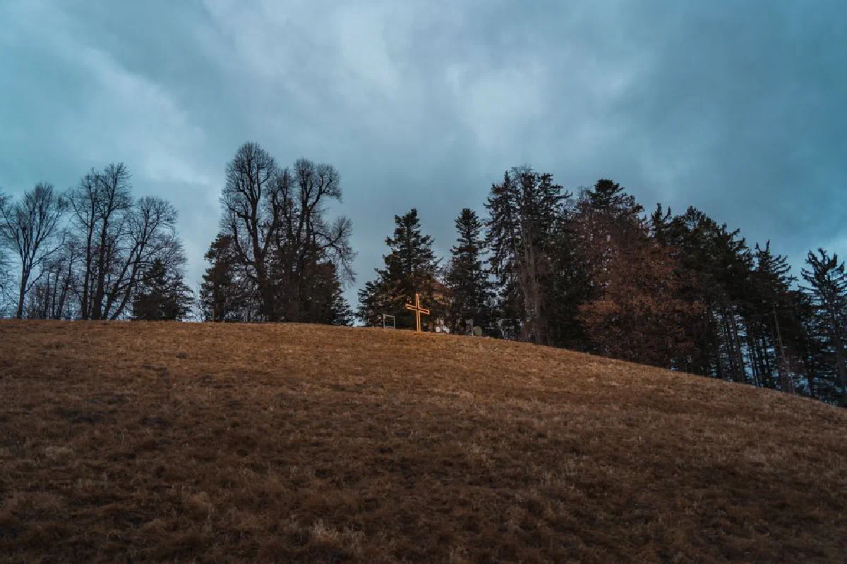A peaceful hilltop with a cross surrounded by autumn trees under a cloudy sky.