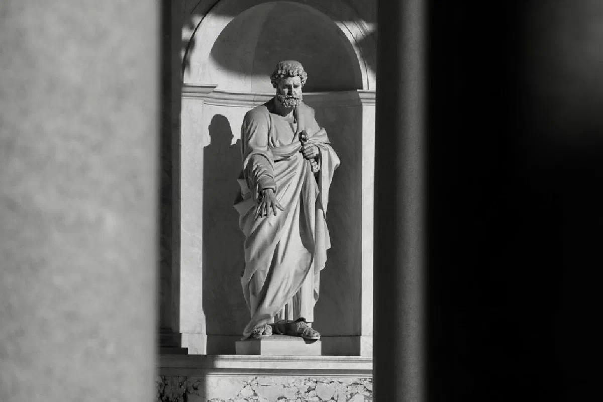 A monochrome photograph of an ancient marble statue in a historic Roman setting.