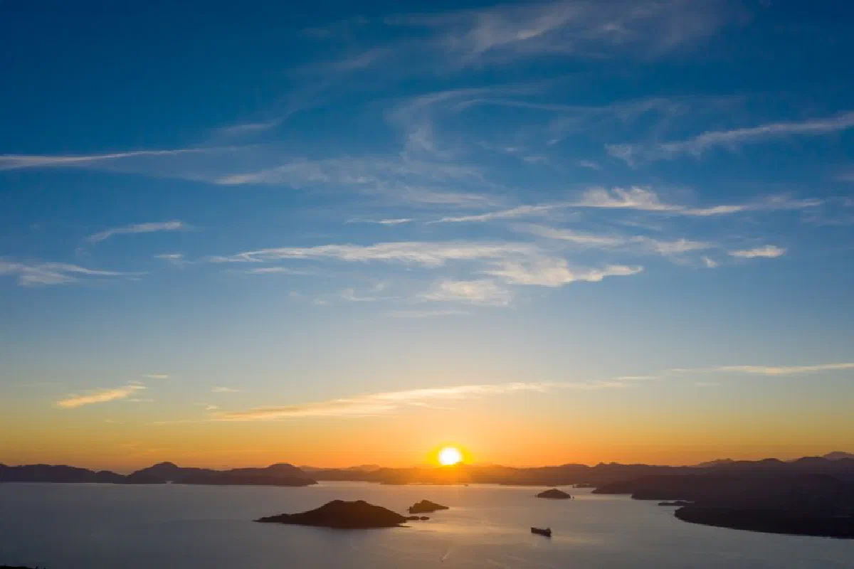 A stunning sunset over a calm ocean with silhouetted islands and vibrant skies.