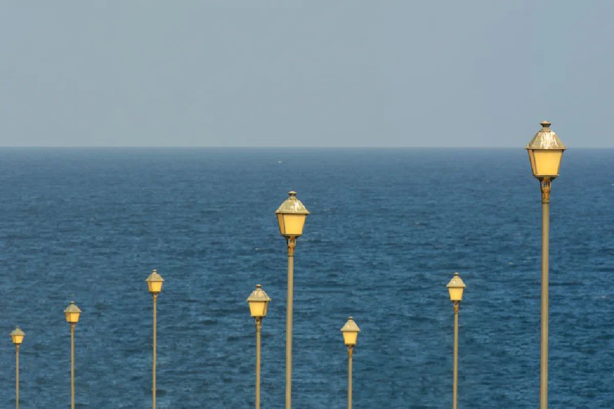Street lamps lined up along a coastline with a vast ocean backdrop under a clear summer sky.