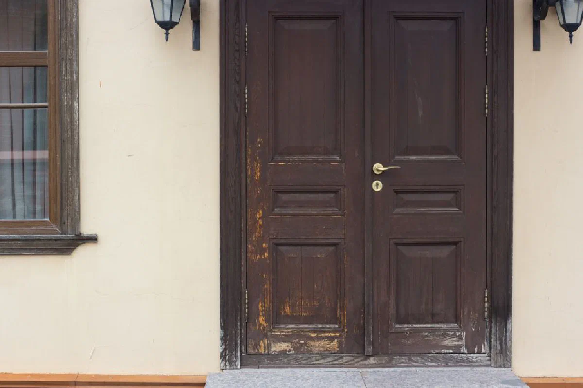A rustic wooden double door entrance with vintage lanterns, showcasing traditional architectural style.