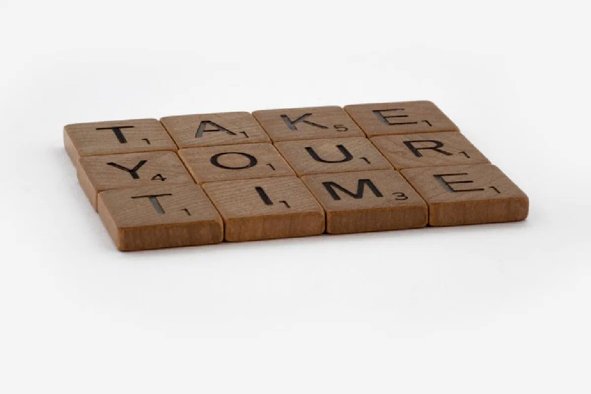 Scrabble tiles spelling 'Take Your Time' on a white background, promoting patience.